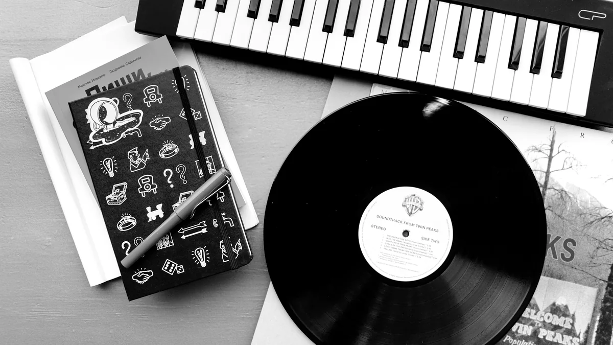 A vinyl record, notebook and keyboard arranged on a music desk.